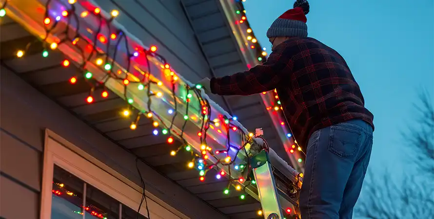 Man on ladder hanging holiday lights